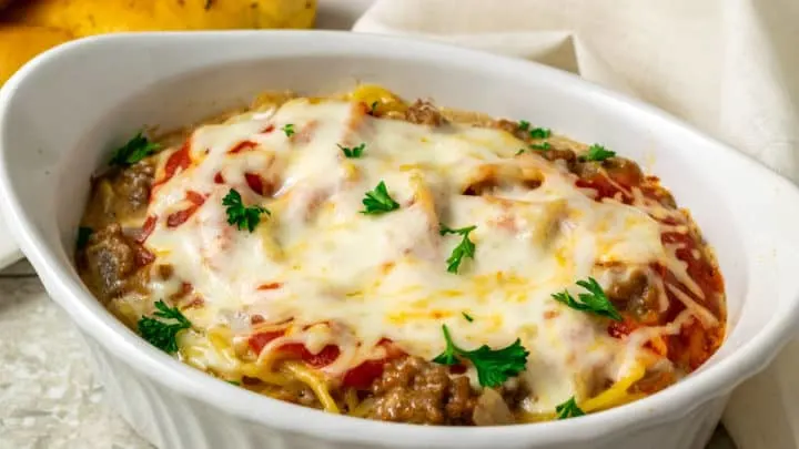 a baking dish filled with spaghetti noodles, ground beef, red sauce, and cheese and a side of bread sticks