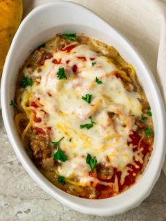 a white baking dish filled with spaghetti noodles, ground beef, red sauce, and cheese