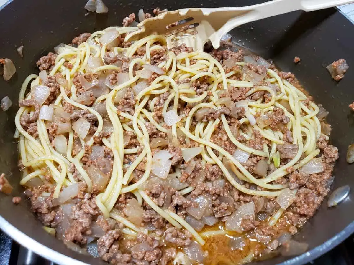 spaghetti noodles added to beef mixture cooking in a frying pan