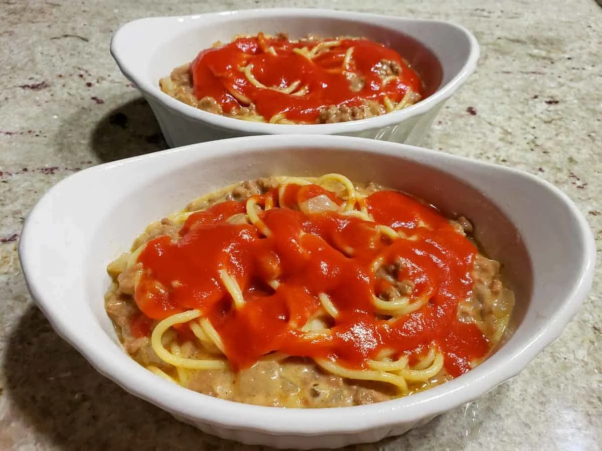 spaghetti casserole topped with red sauce in two dishes