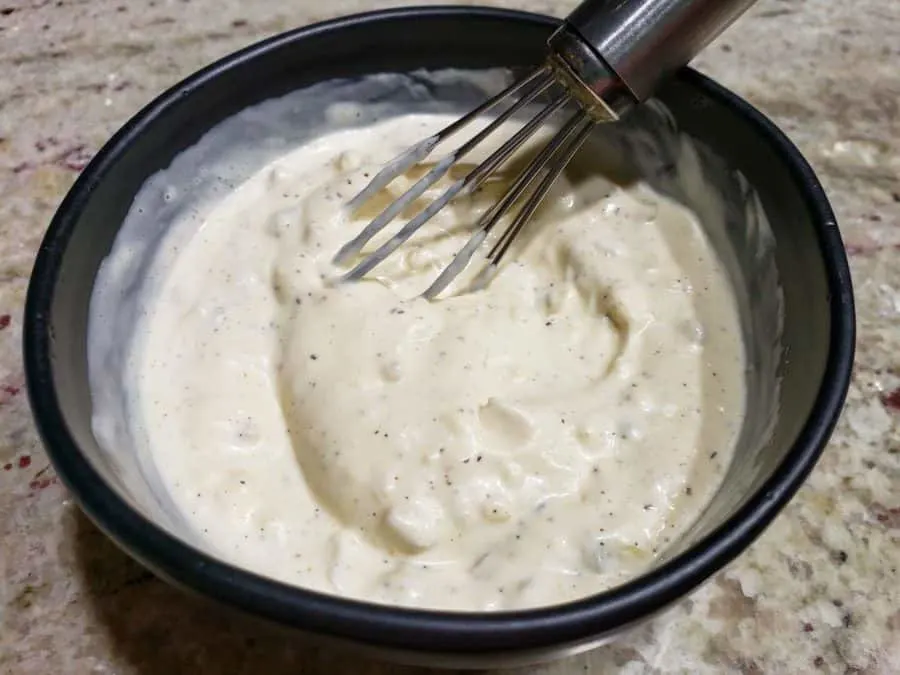a bowl filled with white creamy sauce and a whisk.