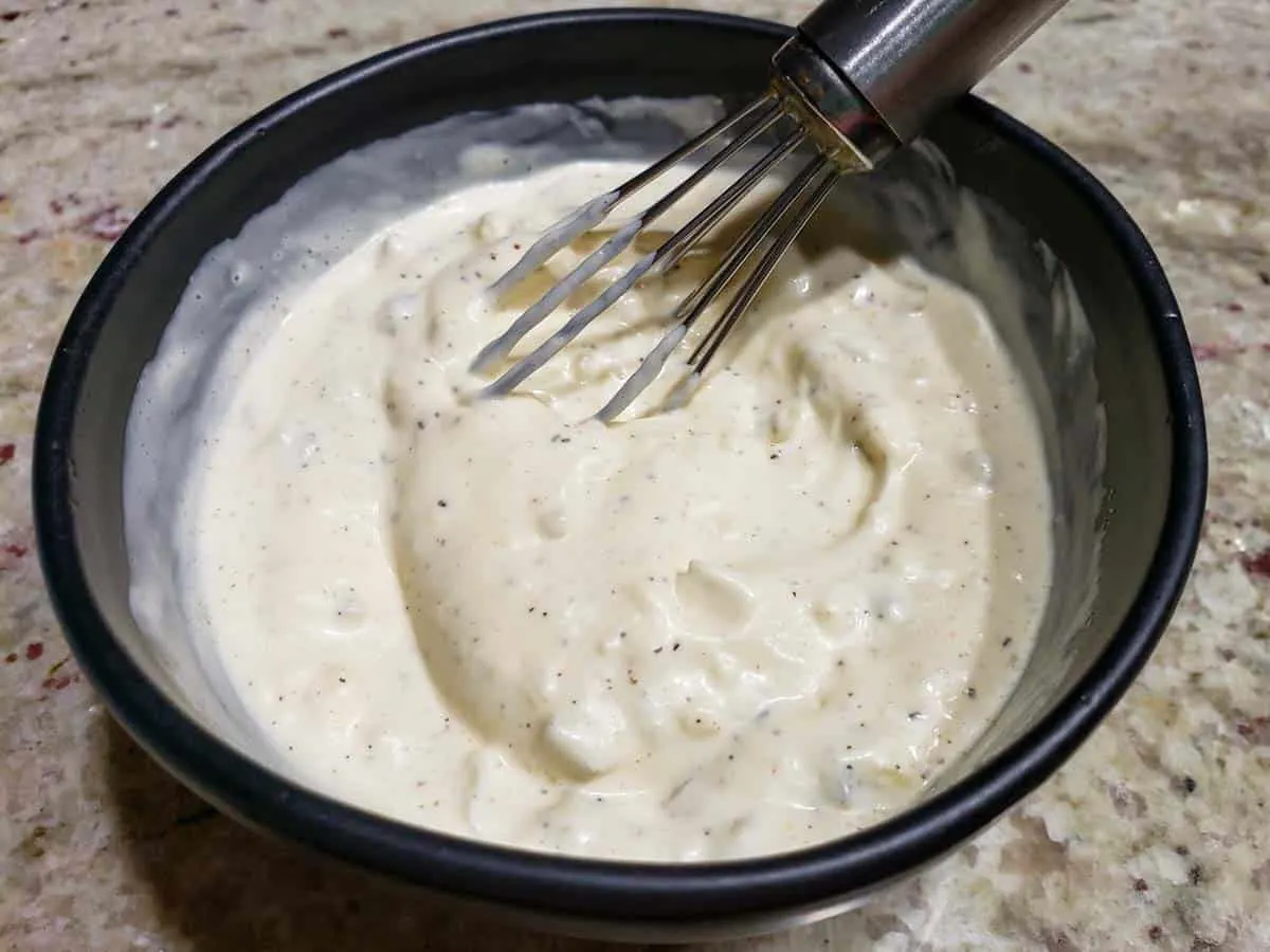 a bowl filled with white creamy sauce and a whisk