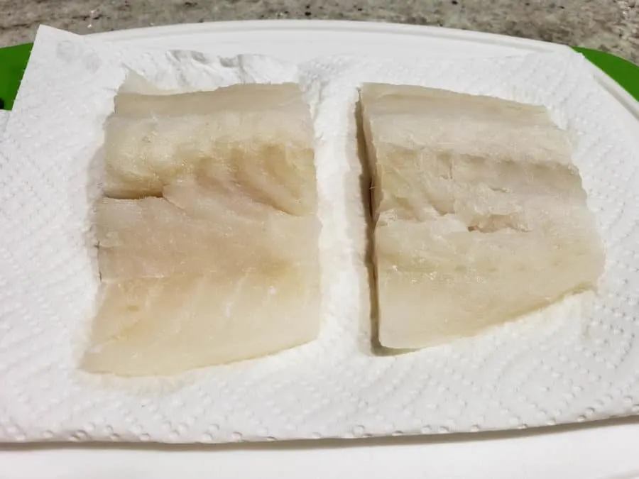 two cod fish fillets drying on paper towel.