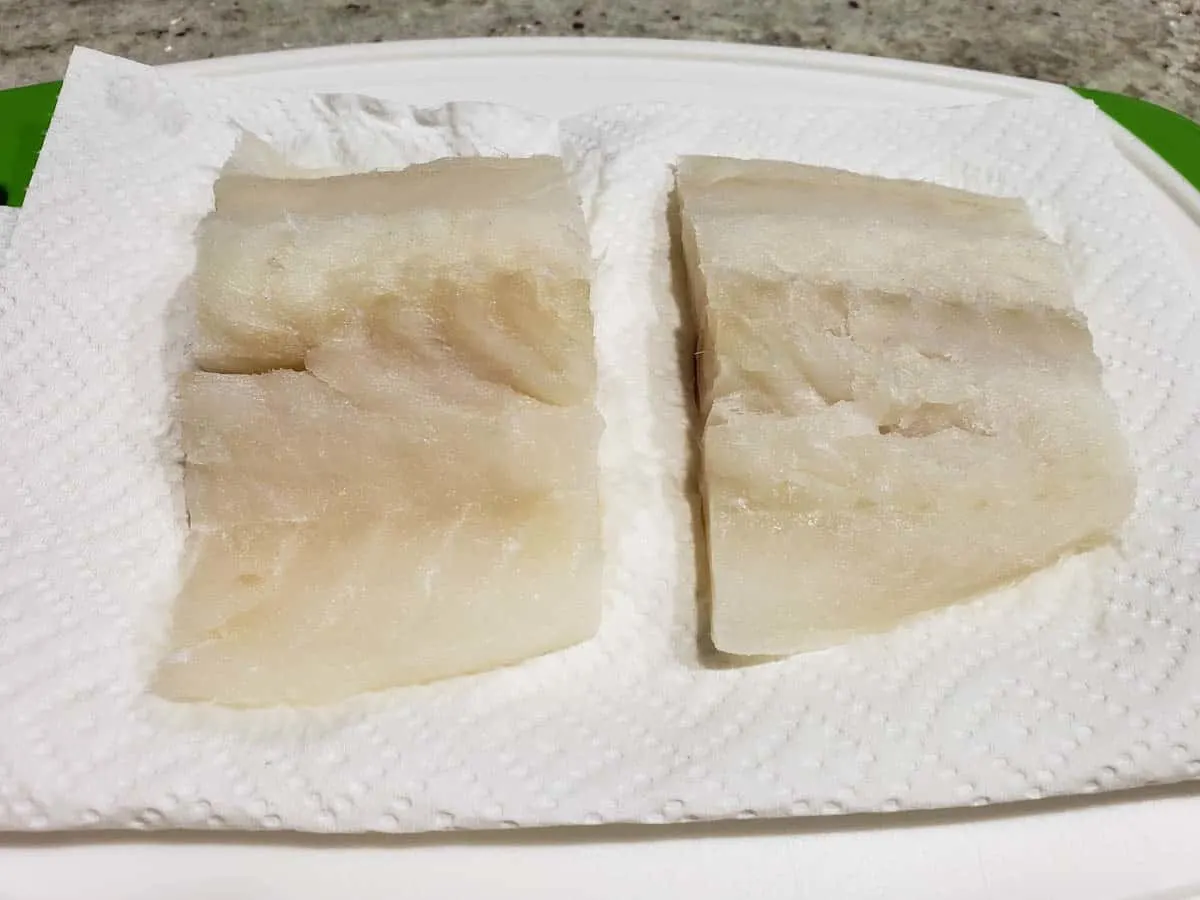 two cod fish fillets drying on paper towel