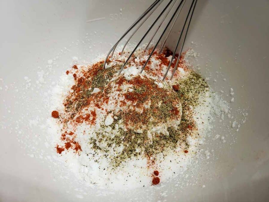 a bowl filled with flour, seasonings, and a whisk.