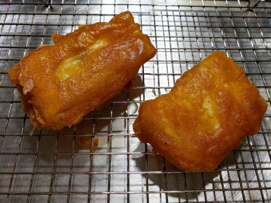 two golden brown beer battered cod fish draining on a wire rack.