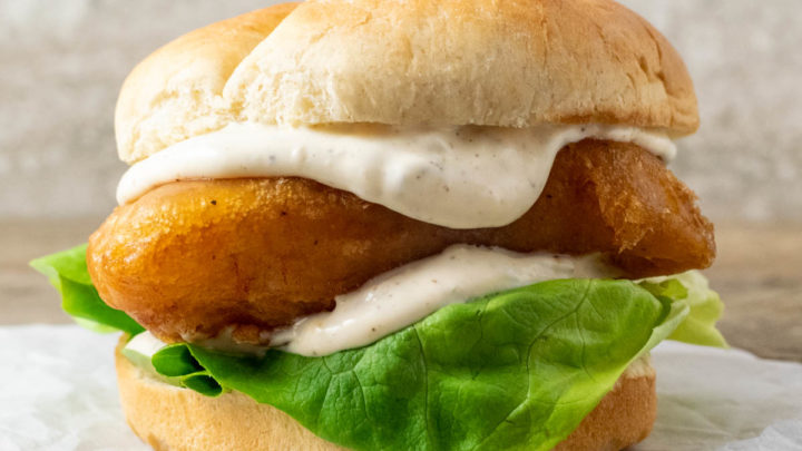 up close front view of a bun filled with lettuce, white creamy sauce, and golden brown fish filet