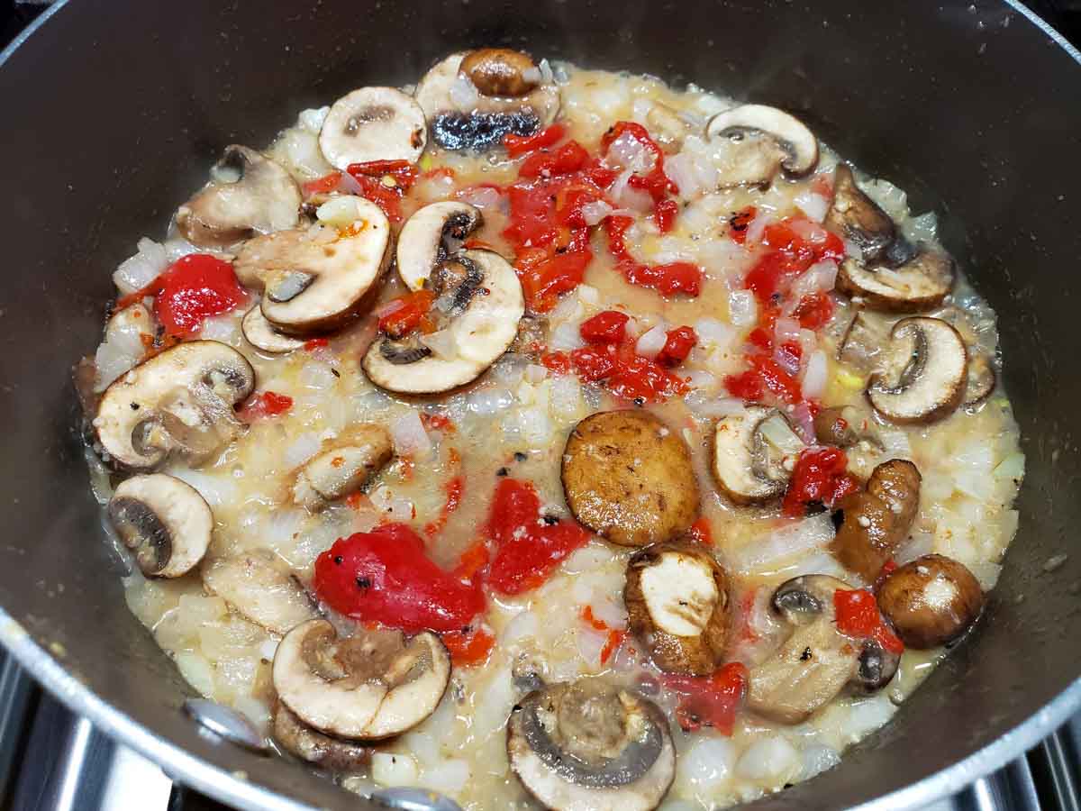 a pan filled with mushrooms, roasted red peppers, and onions in a yellow butter sauce