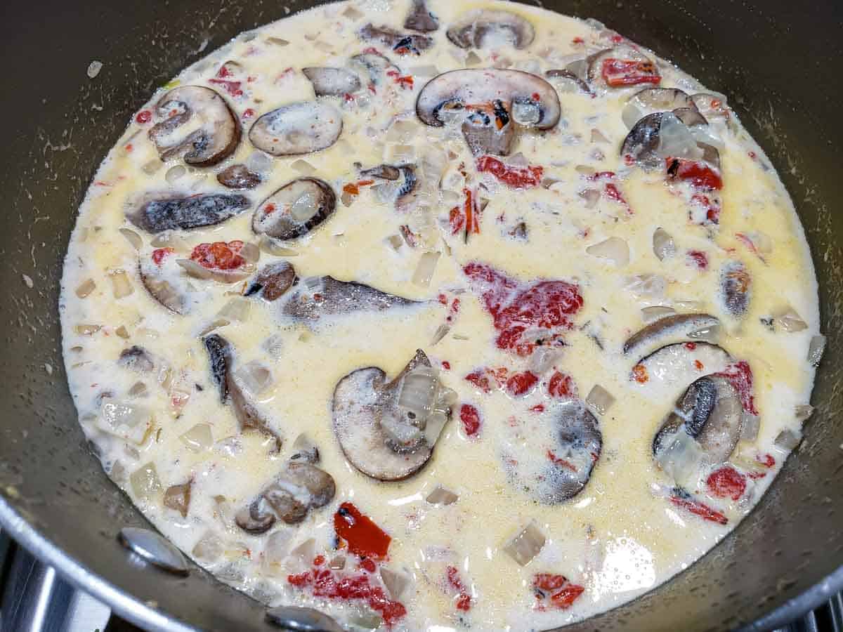 a pan filled with mushrooms, roasted red peppers, and onions in a creamy white sauce