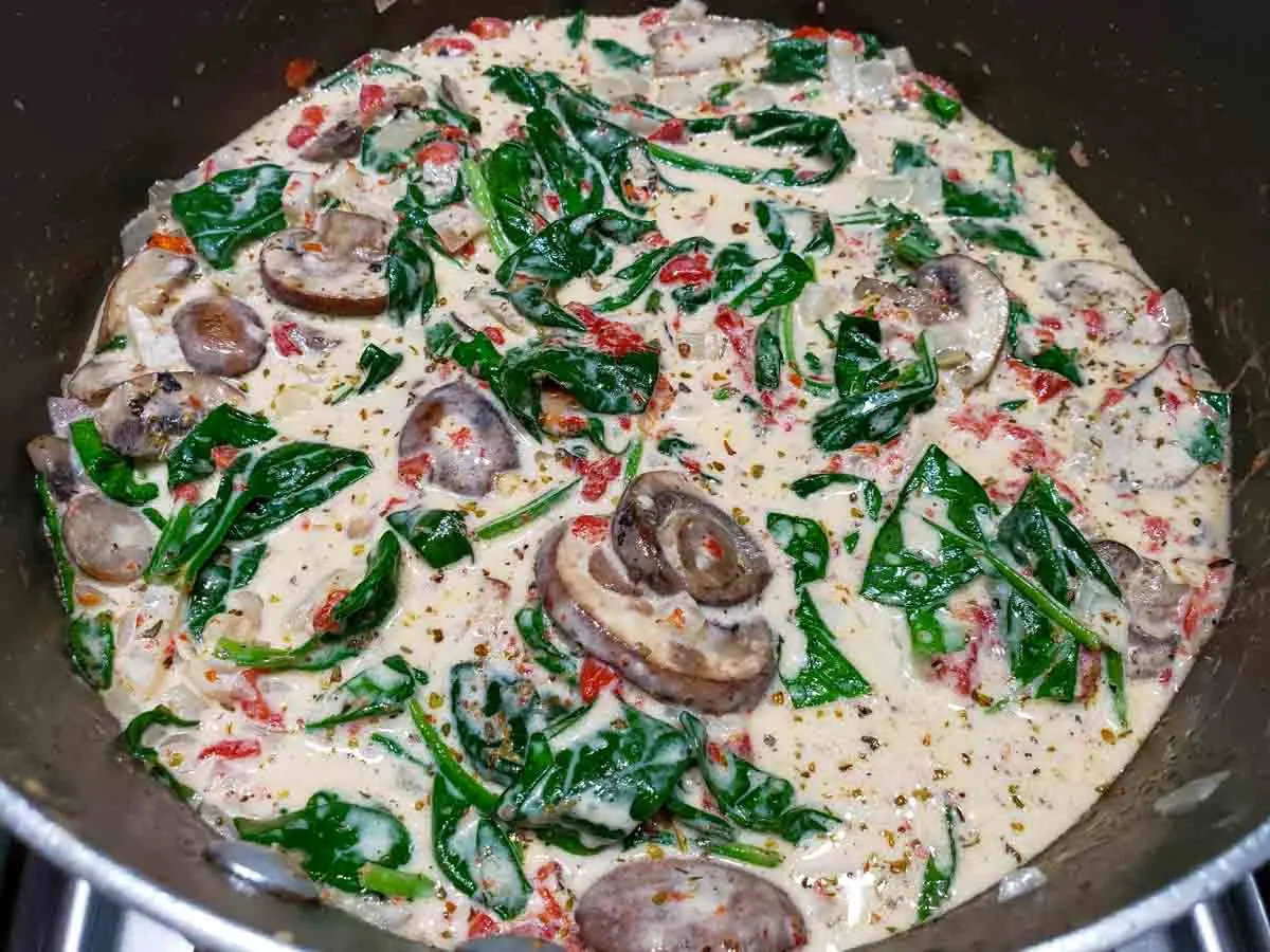 a pan filled with mushrooms, roasted red peppers, spinach and onions in a yellow butter sauce