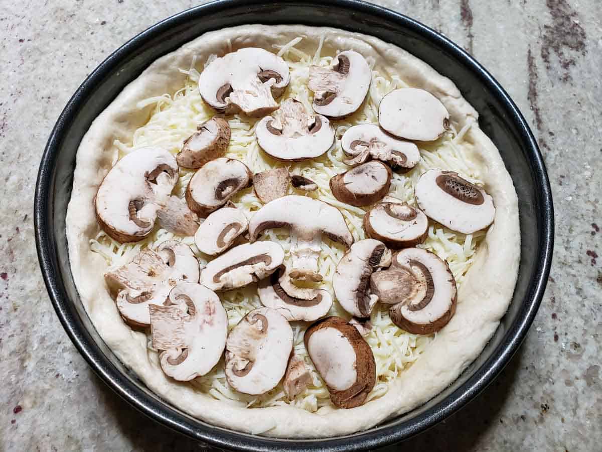 homemade pizza dough in a springform pan and filled with mozzarella and sliced mushrooms.