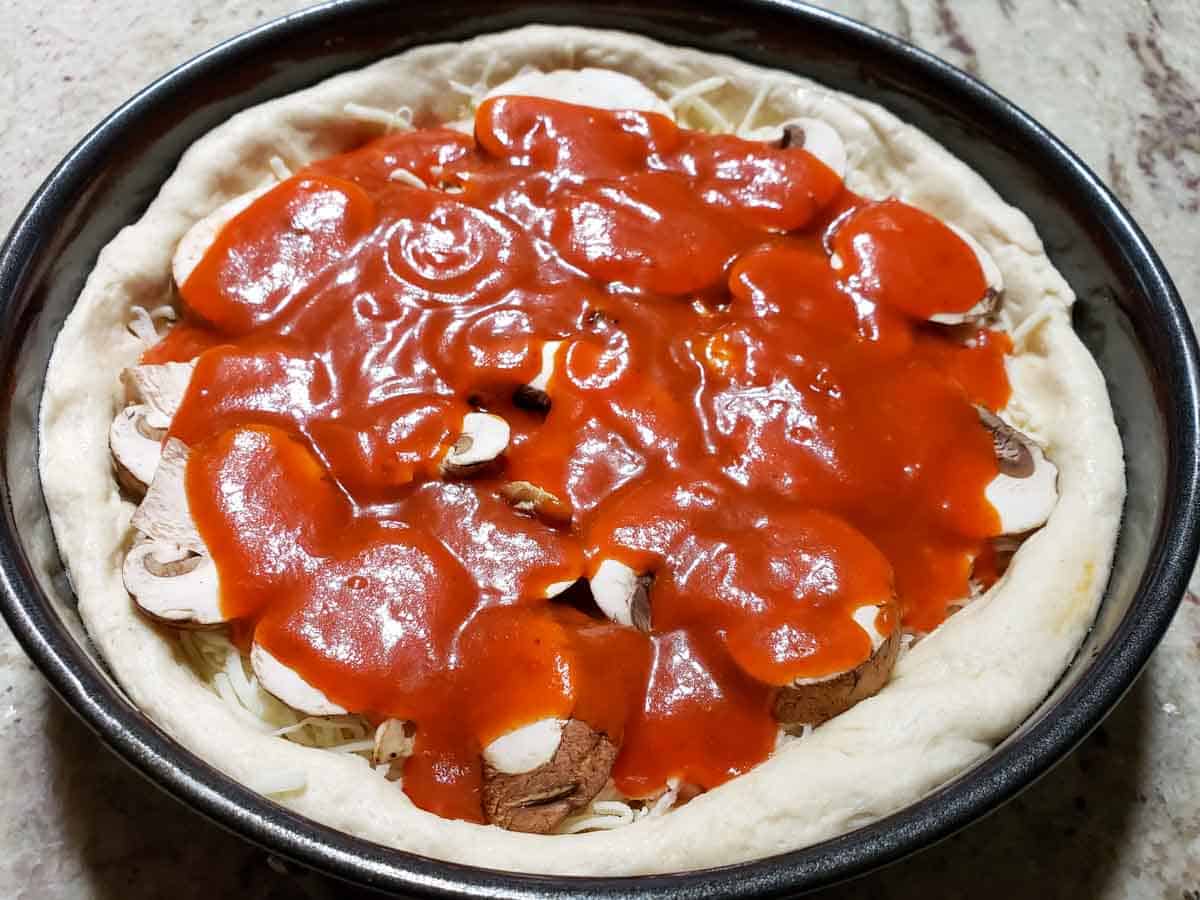 red pizza sauce added to the top of an unbaked deep dish pizza.