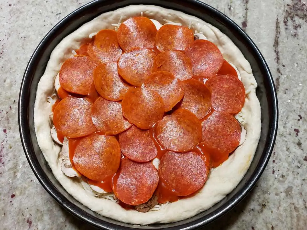 pepperoni slices added to the top of an unbaked deep dish pizza.