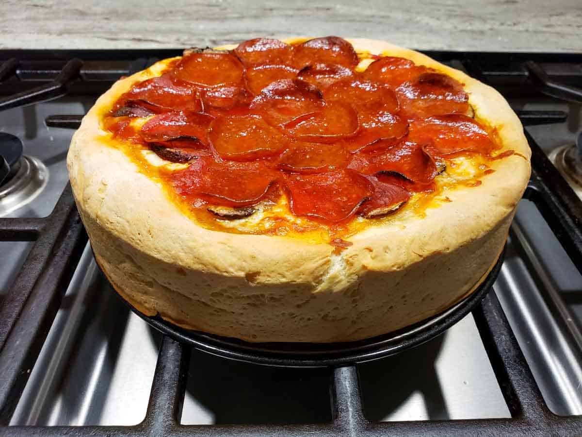 a baked deep dish pizza cooling on a stove.