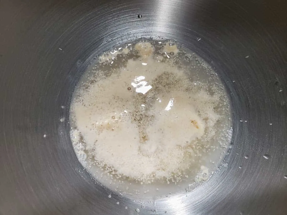 a silver bowl filled with foamy yeast activating in water and sugar