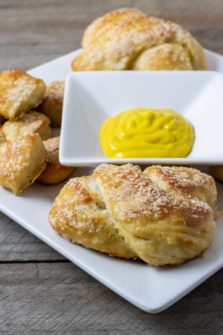 a white plate filled with homemade soft pretzels and pretzel bites and a bowl of mustard in the middle