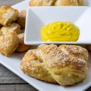 a white plate filled with homemade soft pretzels and pretzel bites and a bowl of mustard in the middle