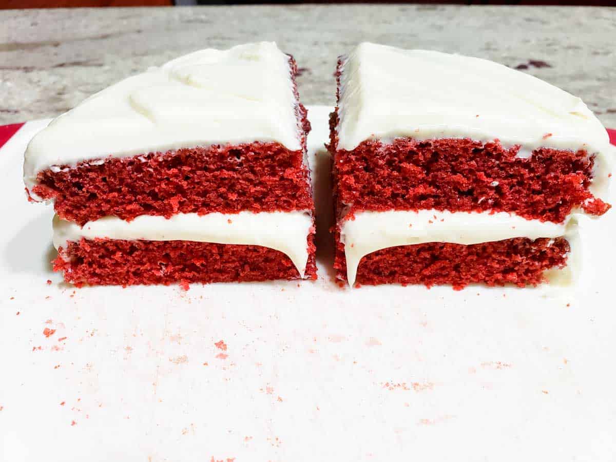 two slices of two layer red velvet cake with cream cheese frosting on a cutting board