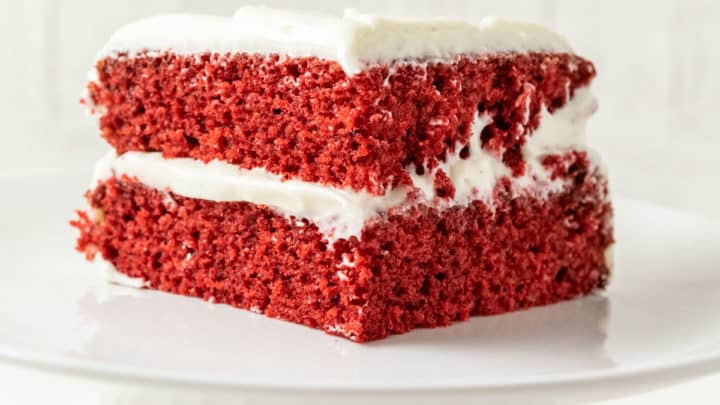 a white cake stand with a piece of two layer red cake with white creamy frosting