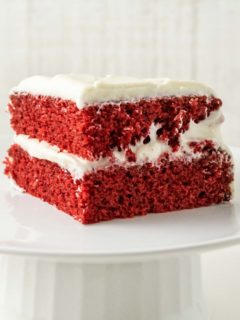a piece of two layer red cake with white frosting on top of a cake stand