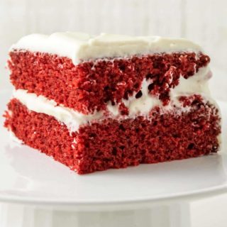 a piece of two layer red cake with white frosting on top of a cake stand