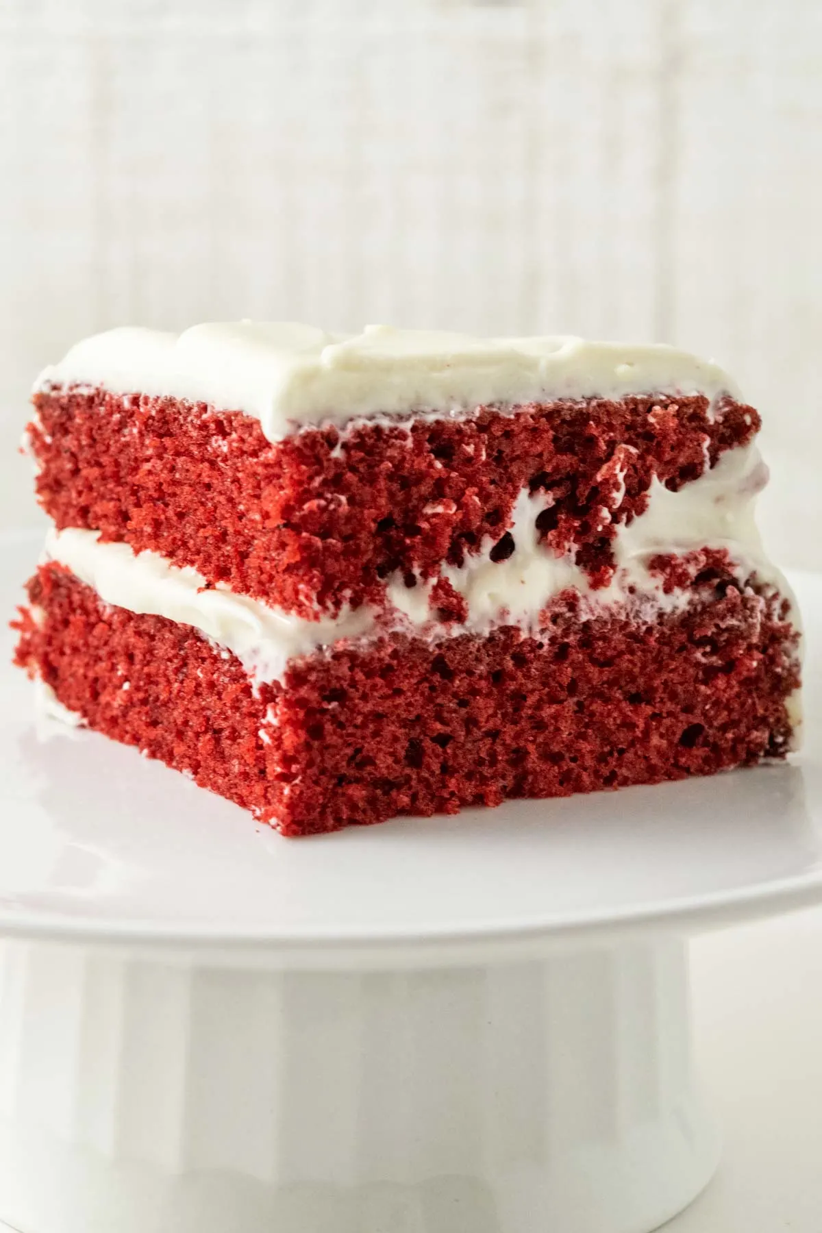 a piece of two layer red cake with white frosting on top of a cake stand