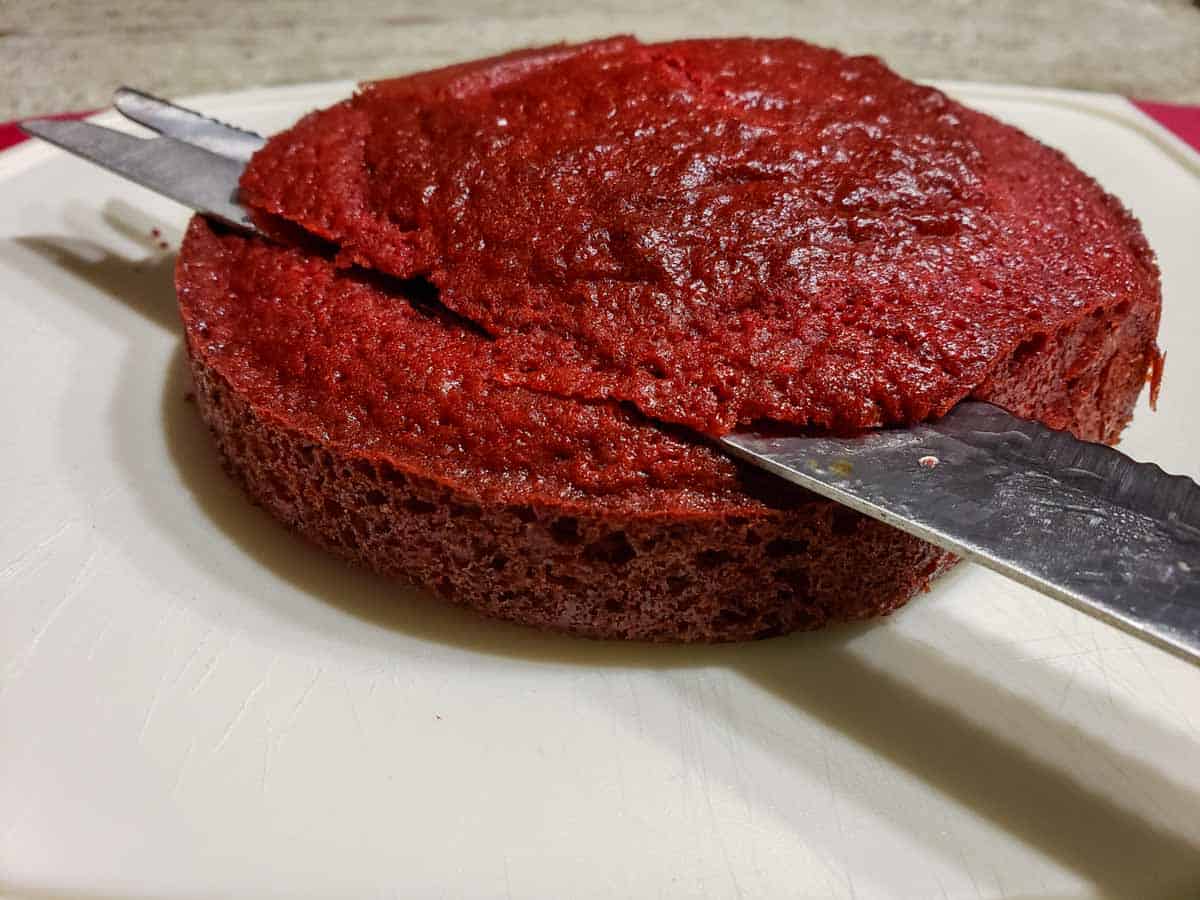 a red velvet cake with a knife slicing the top rounded part off