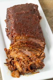 a half sliced Slow Cooker Beef brisket with BBQ Sauce on a white platter