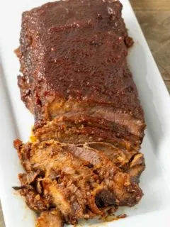 a half sliced Slow Cooker Beef brisket with BBQ Sauce on a white platter