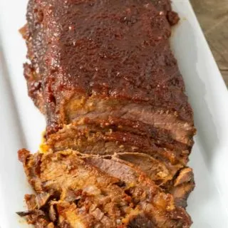 a half sliced Slow Cooker Beef brisket with BBQ Sauce on a white platter