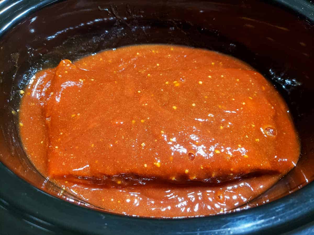 a crockpot filled with beef brisket and orange bbq sauce