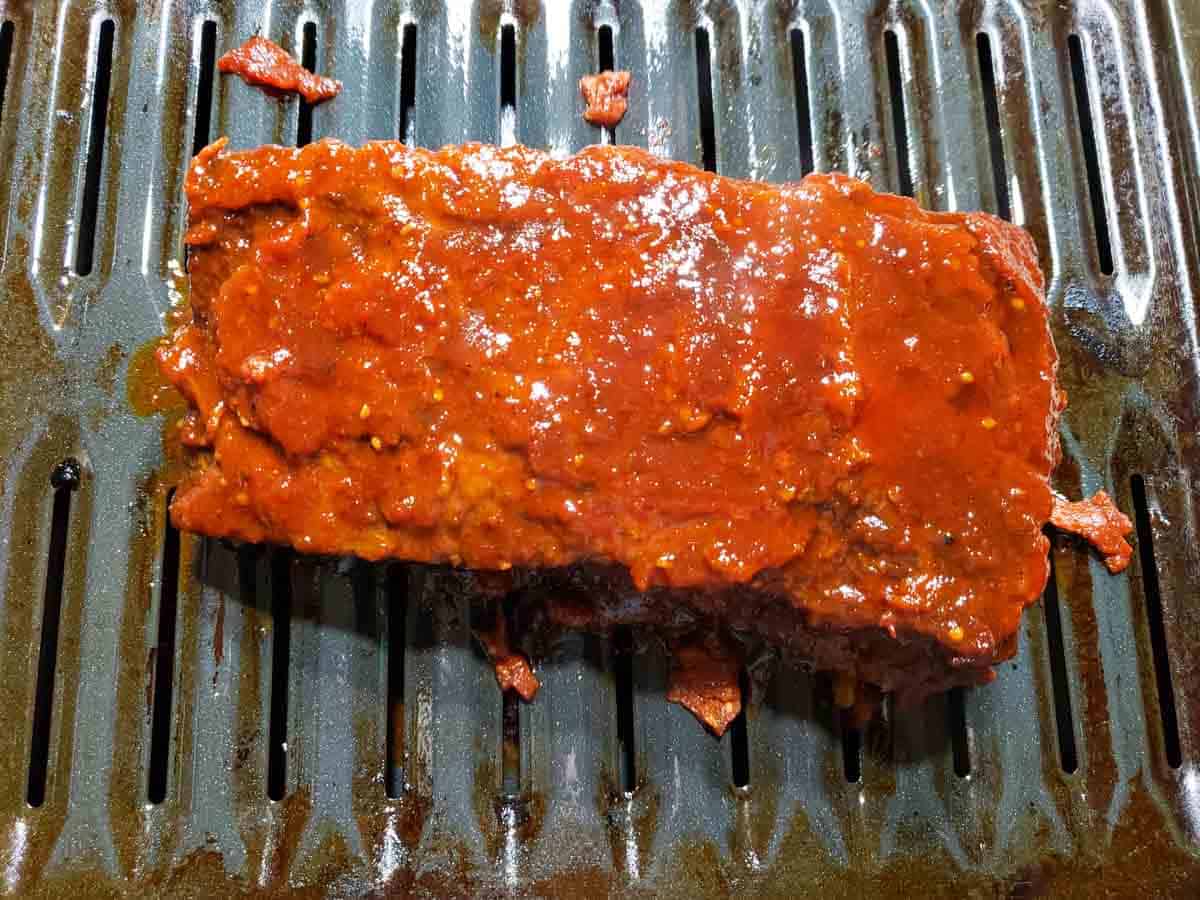 a cooked beef brisket covered in orange bbq sauce on a broiler pan