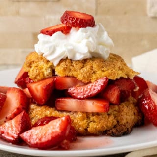close up front view of a plate filled with a golden brown biscuit topped with sliced strawberries, red juice, and whipped cream