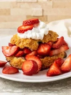 a white plate plate filled with a golden brown biscuit topped with sliced strawberries, red juice, and whipped cream
