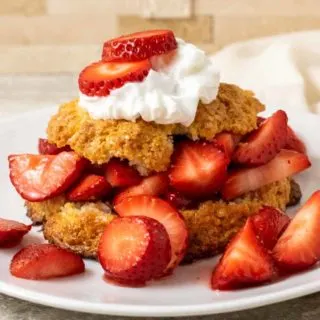 a white plate plate filled with a golden brown biscuit topped with sliced strawberries, red juice, and whipped cream