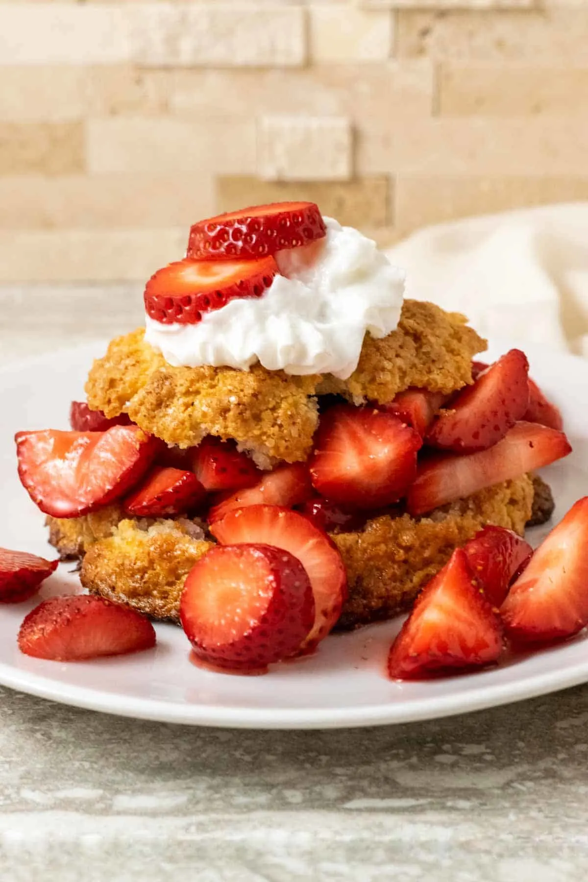 a white plate plate filled with a golden brown biscuit topped with sliced strawberries, red juice, and whipped cream