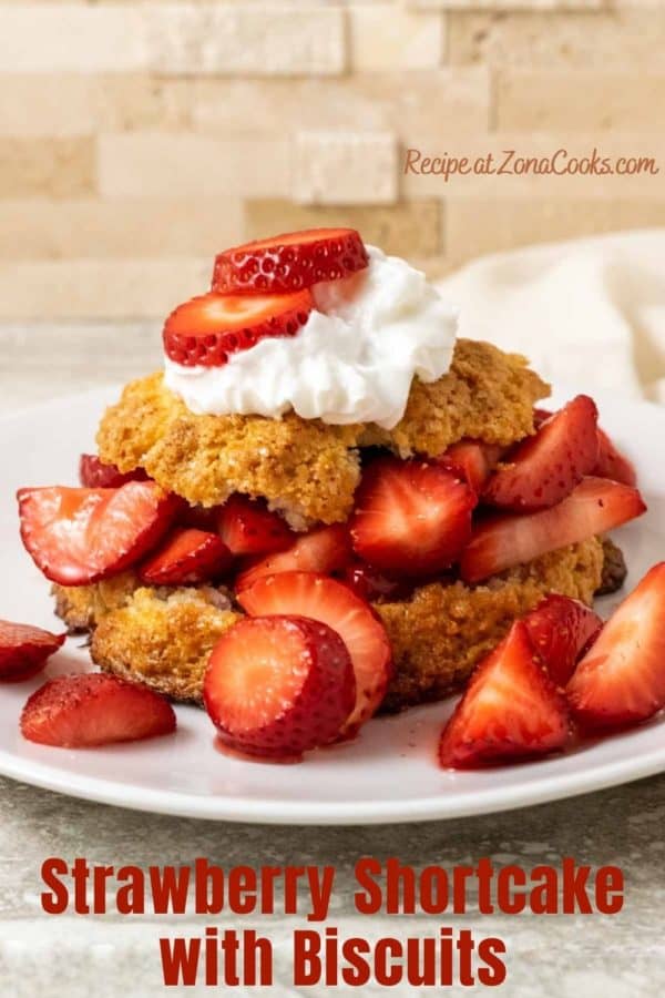 a plate filled with a golden brown biscuit topped with sliced strawberries, red juice, and whipped cream and text saying strawberry shortcake with biscuits recipe at zonacooks.com