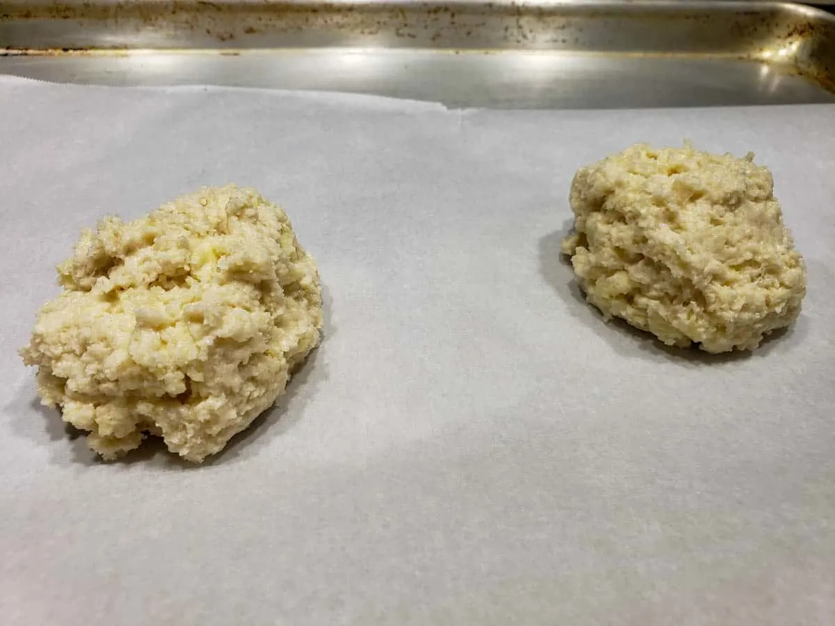 two sticky buttermilk biscuit dough balls dropped on a baking sheet
