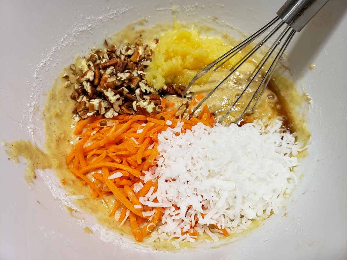 carrots, coconut, and pecans added to cake batter in a bowl