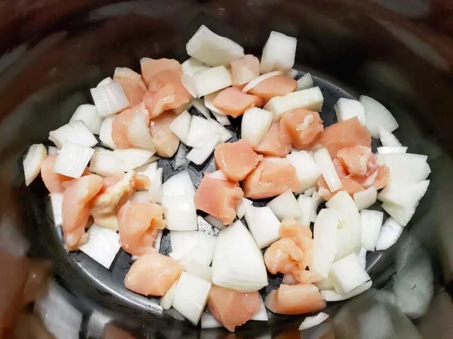 a crock pot filled with diced onions and diced raw chicken