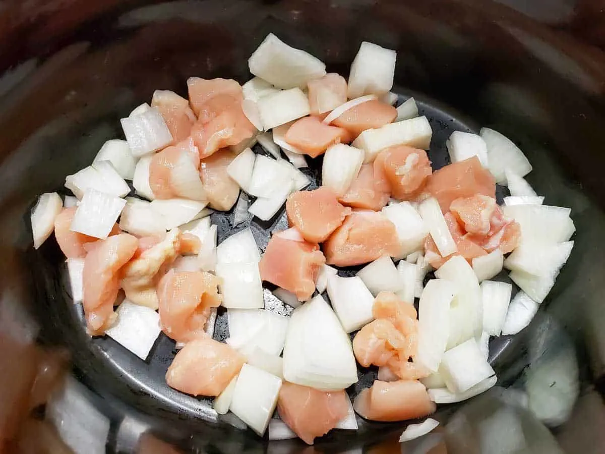 a crock pot filled with diced onions and diced raw chicken.