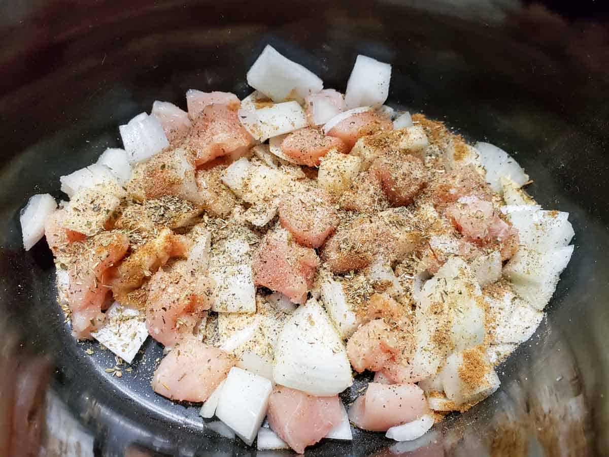 a slow cooker crock pot filled with diced onions and diced raw chicken and seasonings.