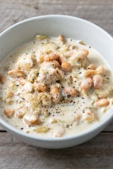 a bowl filled with northern beans, chicken, and diced chiles in white liquid