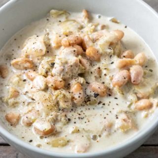 a bowl filled with northern beans, chicken, and diced chiles in white liquid