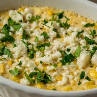 an up close view of a casserole dish filled with corn, white cheese, chopped cilantro and creamy sauce