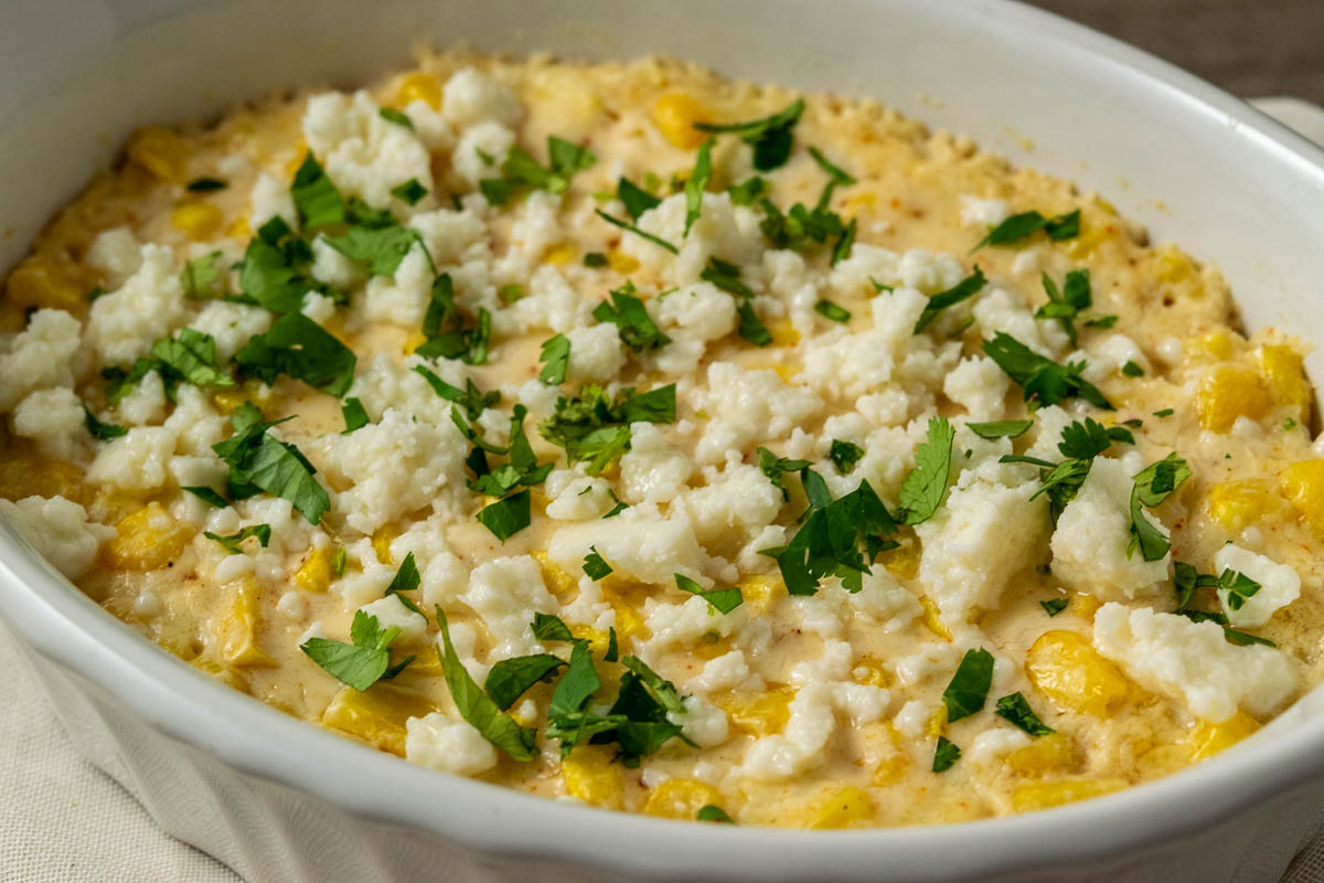 an up close view of a casserole dish filled with corn, white cheese, chopped cilantro and creamy sauce