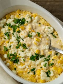 a casserole dish filled with corn, white cheese, chopped cilantro and creamy sauce with a spoon lifting some out