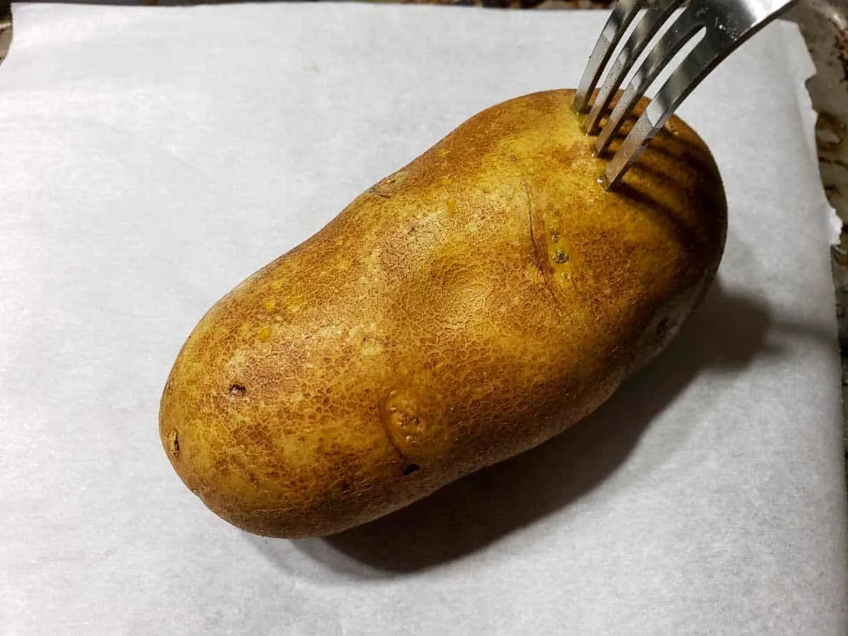 a brown potato with a fork poking holes into it
