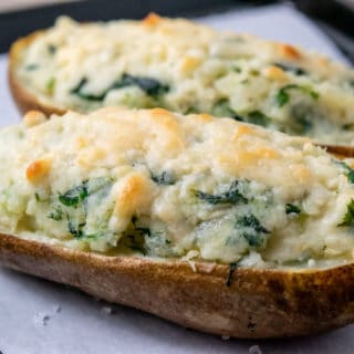 a close up view of two potatoes filled with mashed potato, cream cheese, and spinach with parmesan cheese browned on top
