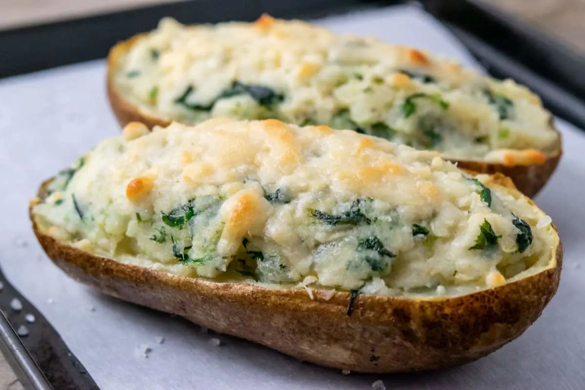 a close up view of two potatoes filled with mashed potato, cream cheese, and spinach with parmesan cheese browned on top
